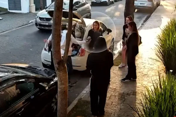Imagem colorida em que três homens armados rendem cinco mulheres em frente a um carro
