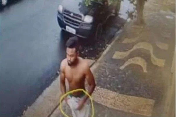 Imagem colorida de homem sem camisa carregando objeto embrulhado que parece uma arma - Metrópoles
