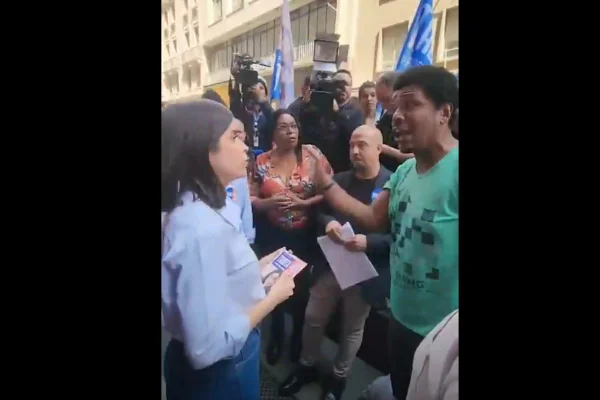 imagem colorida mostra candidata tabata amaral conversando com homem em situação de rua. ela é branca, veste uma camisa azul claro e segura folhetos nas mãos. O homem é negro, veste uma camiseta verde e gesticula com o braço