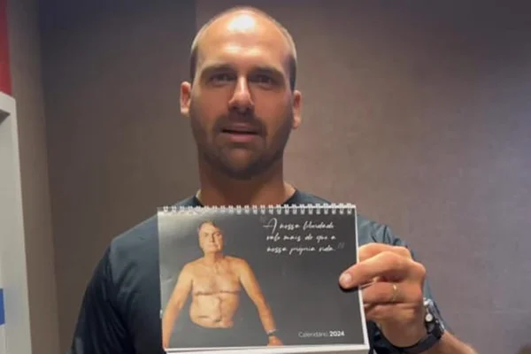 Imagem colorida mostra eduardo bolsonaro expondo foto de calendário em que Bolsonaro aparece sem camisa - Metrópoles