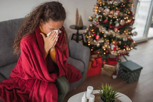 Foto ilustrativa de mulher com alergia com lenço de papel no nariz e árvore de Natal ao fundo - Metrópoles