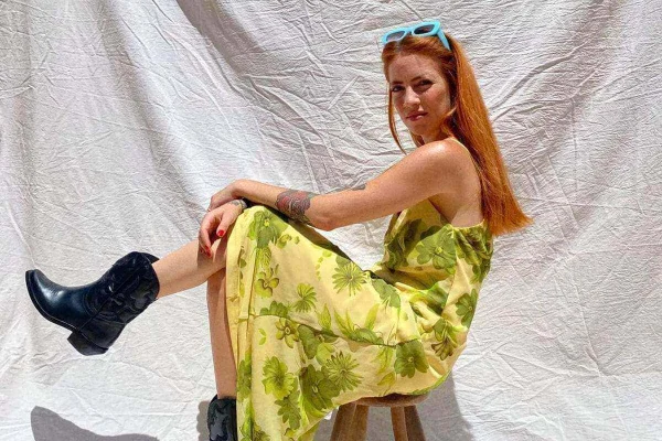 Na imagem com cor, mulher branca com os cabelos ruivos usa vestido estampado e botas pretas - Metrópoles