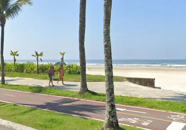 Foto mostra jardim da praia no bairro Jardim Real, em Praia Grande, com dois turistas andando na calçada - Metrópoles