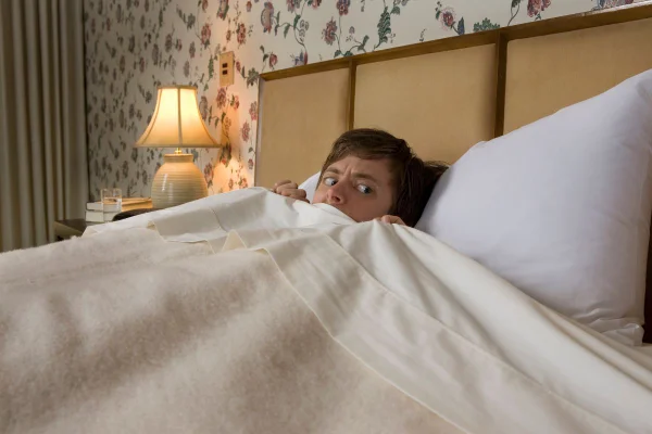 Foto colorida de homem na cama com medo