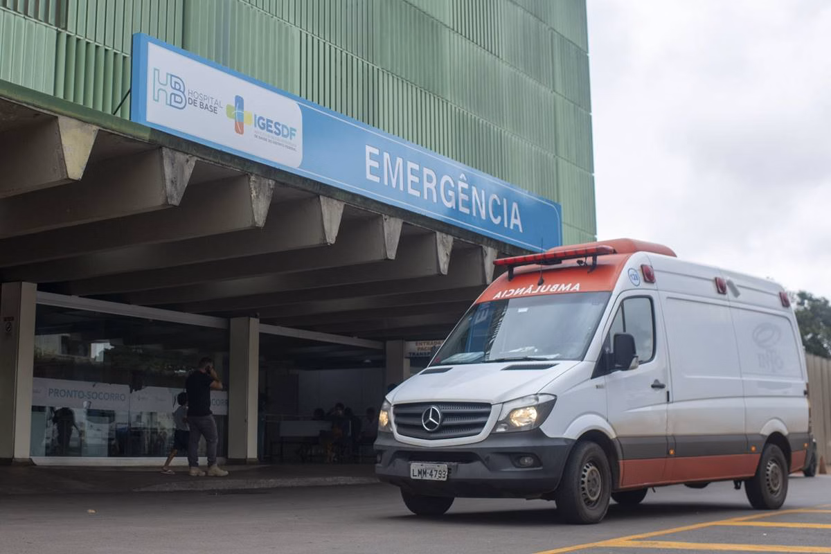 Fachada do Hospital de Base do Distrito Federal, com ambulância na frente de porta da emergência