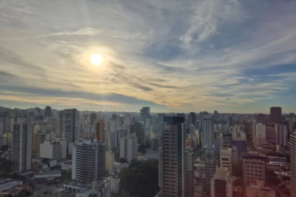 Imagem colorida mostra vista com prédios e sol no céu - Metrópoles