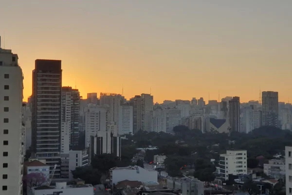 Imagem colorida mostra horizonte de prédios e, ao fundo, o sol nasce - Metrópoles