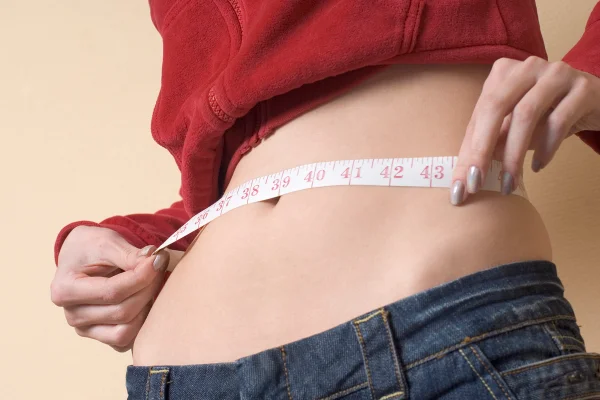 foto colorida de silhueta feminina sendo medida com fita métrica - Metrópoles.