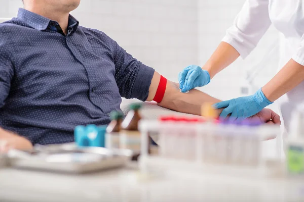 Close de uma enfermeira desinfetando o braço de um homem antes de um exame de sangue. O homem está sentado em uma cadeira perto do conjunto médico.