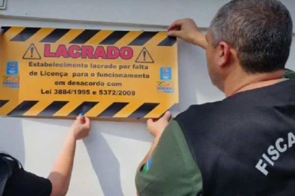 Imagens coloridas mostram homem e mulher, fiscais, colocando uma placa com a inscrição "lacrado" em vermelho para interditar clínica clandestina de reabilitação