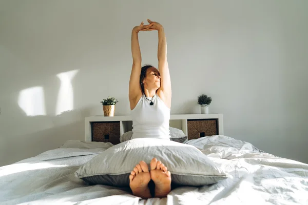 Foto colorida de mulher se espreguiçando na cama após acordar - Psiquiatra ensina 5 melhores hábitos para fortalecer sua saúde mental - Metrópoles