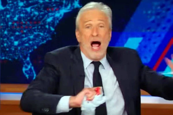 Imagem colorida do apresentador Jon Stewart com a mão cortada - Metrópoles