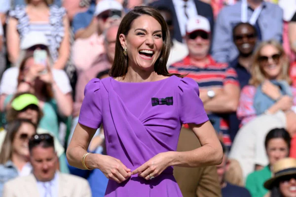 Kate Middleton sorrindo. Ela usa um look roxo - Metrópoles