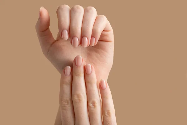 Mãos femininas em um fundo bege. Nas unhas, esmalte em gel nude
