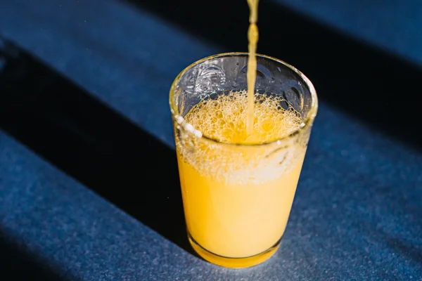 Imagem mostra copo de vidro com suco amarelo em fundo azul - Metrópoles