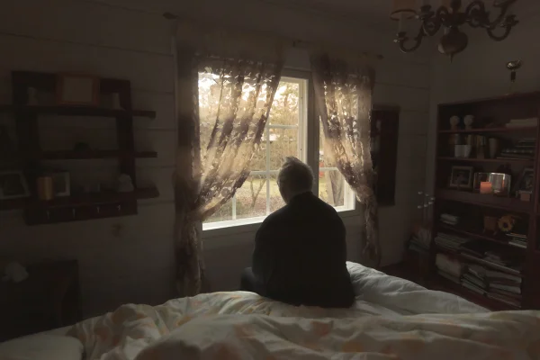 Imagem de idoso sentado na cama olhando para janela - Metrópoles