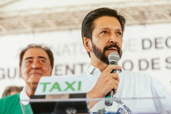 Imagem colorida mostra Ricardo Nunes, homem branco, de cabelo e barba pretos, falando ao microfone - Metrópoles
