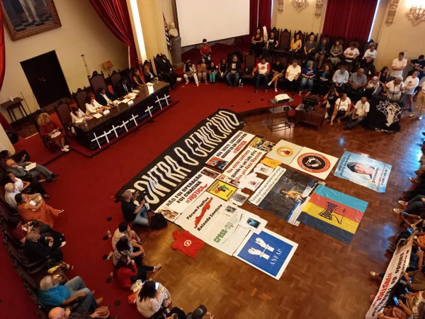 Imagem mostra faixas em auditório e pessoas sentadas nas cadeiras - Metrópoles