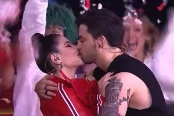 Gkay, com um casaco vermelho e pele clara, beija Felipe Neto, homem de pele clara, regata preta e cabelo preto - Metrópoles