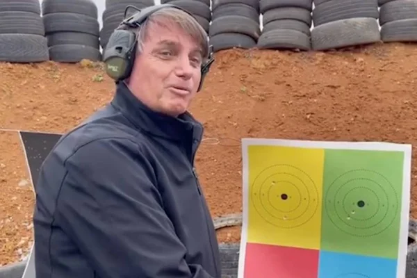 Bolsonaro treina tiro ao alvo com arma de fogo. O alvo é colorido, à sua frente, e ele usa jaqueta preta e abafador - Metrópoles