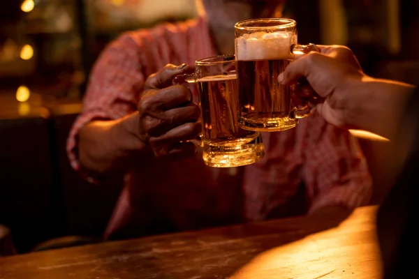 Homens idosos felizes brindando com copos de cerveja em pub. Metrópoles