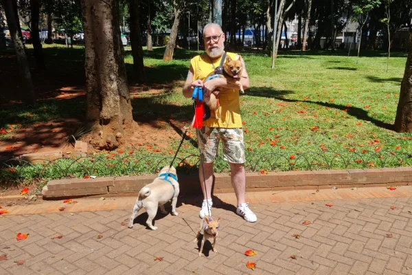 Imagem colorida de um homem de barba com braços cruzado e seus dois cachorros ao seu lado. Metrópoles