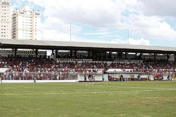 Imagem mostra o gramado e, ao fundo, as arquibancadas de um estádio pequeno de futebol, a Rua Javari