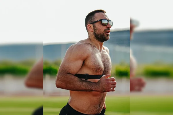 Imagem colorida de um homem sem camisa e de óculos, correndo. Ao fundo, um gramado verde