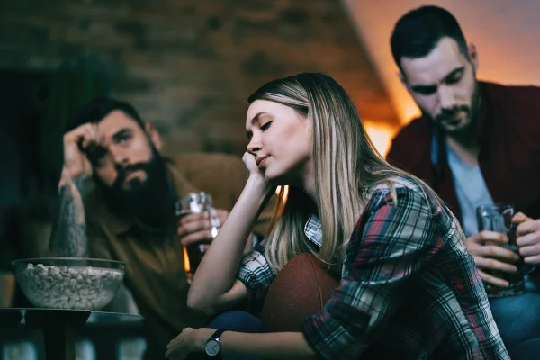 Foto colorida de mulher com cara de frustração ao lado de dois homens