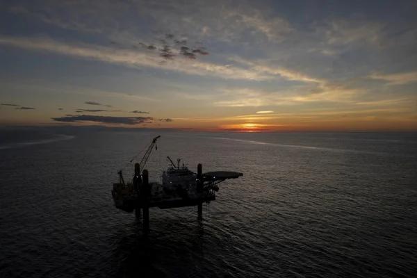 Foto colorida de uma plataforma instalada no meio do oceâno e ao fundo um pôr do sol - Metrópoles.