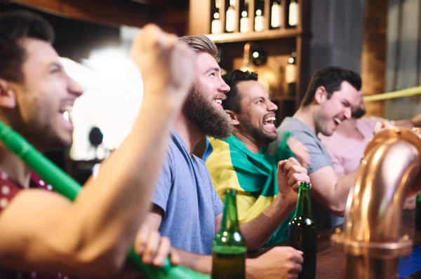 Na imagem, vários homens torcendo para o Brasil em um bar
