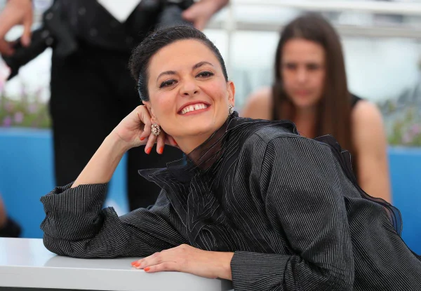 foto colorida de mulher branca sorrindo apoiada em mesa de blusa preta - metrópoles