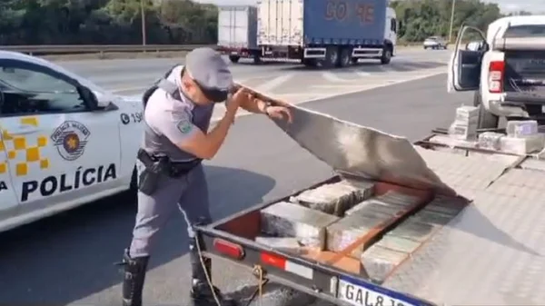 Imagem colorida mostra policial abrindo reboque de carreta. Dentro dele, estão vários pacotes de cocaína - Metrópoles