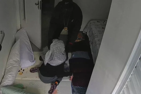 Homem vestido de preto cobre com lençol cabeça de jovem sentado no chão - Metrópoles