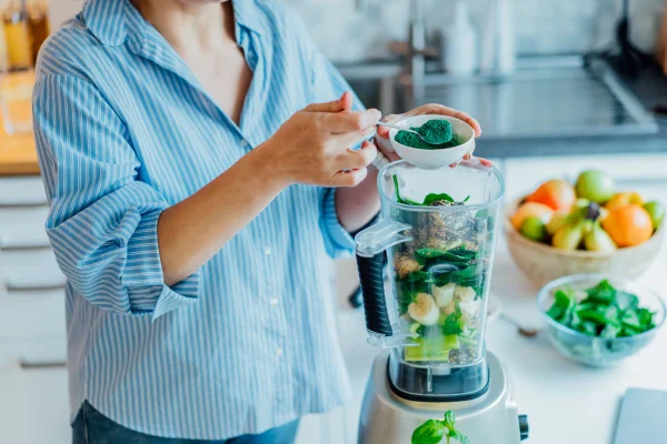 Foto colorida de mulher fazendo uma vitamina e usando a cianobactéria spirulina