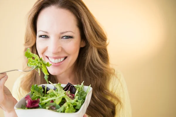 Mulher branca, de cabelos longos e claros está sorrindo e segurando um recipiente com saladas - Metrópoles