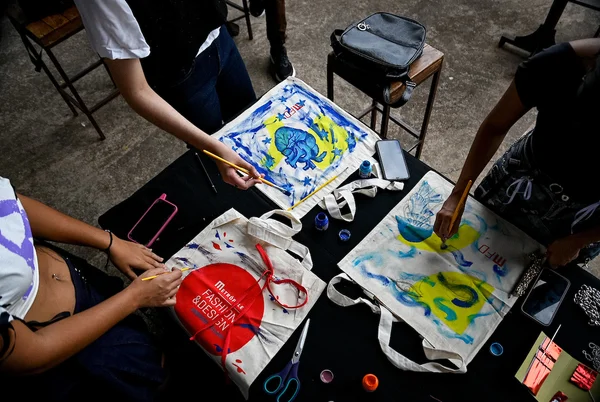 A imagem mostra pessoas pintando em ecobags