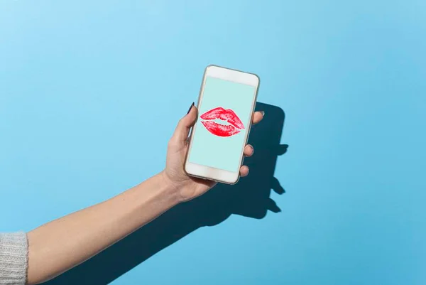 Mão segurando celular com desenho de beijo na tela - Metrópoles