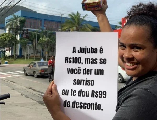 foto colorida da ambulante Bruna Correia, com cartaz em que anuncia que dá descontos em seus doces para quem sorrir - Metrópoles