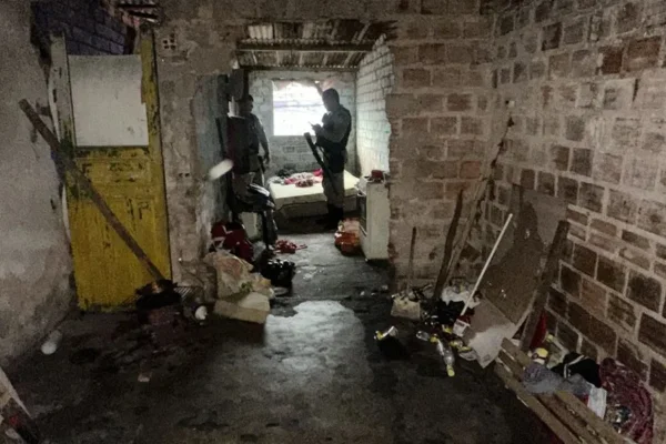Foto colorida de uma casa velha que servia de cativeiro e agentes policiais