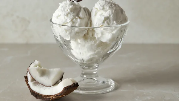 Foto colorida de sorvete de coco em taça com fruta ao lado