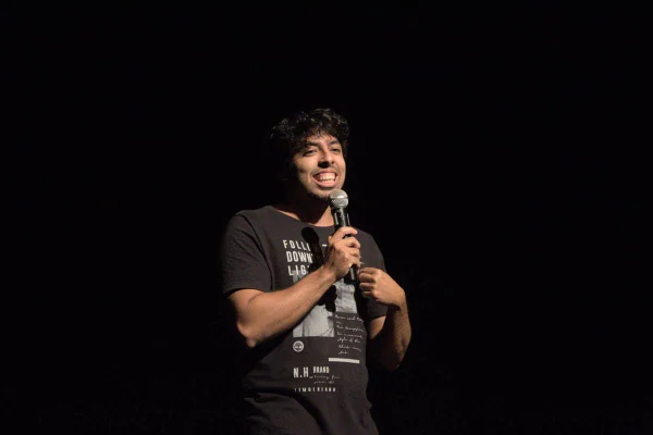 Foto de um homem negro falando em um microfone. O fundo é preto - Metrópoles