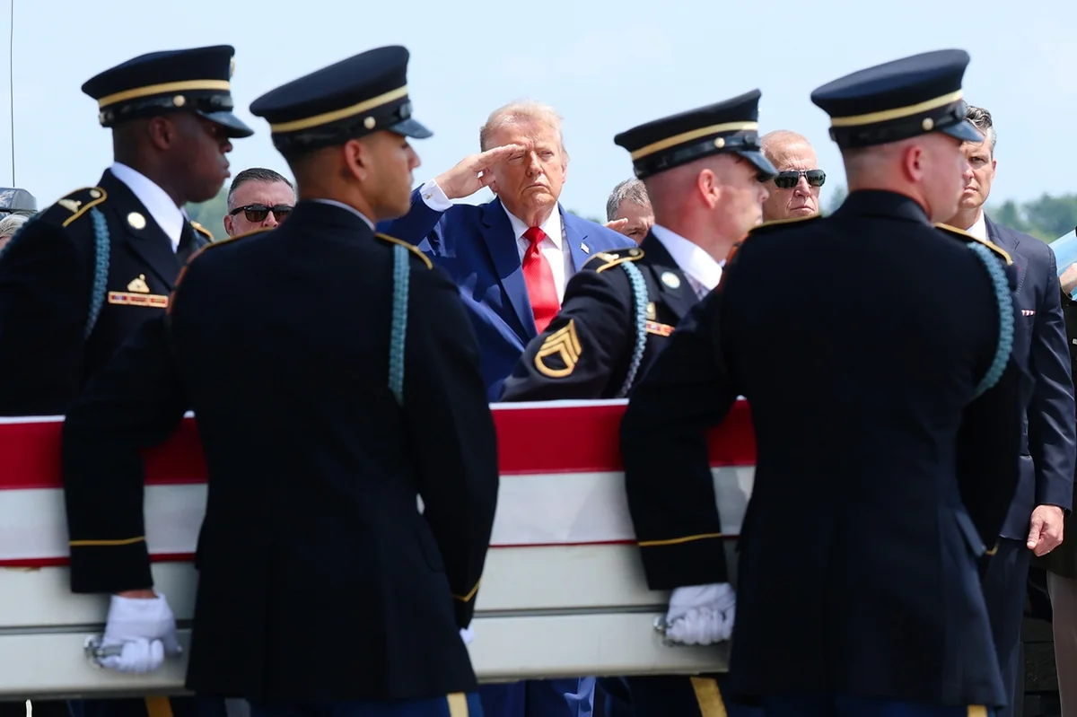 O presidente dos EUA, Donald Trump (ao centro), presta continência enquanto membros de uma equipe de transporte do Exército dos EUA conduzem o caixão de traslado — coberto pela bandeira americana O presidente dos EUA, Donald Trump (ao centro), presta continência enquanto membros de uma equipe de transporte do Exército dos EUA conduzem o caixão de traslado — coberto pela bandeira americana