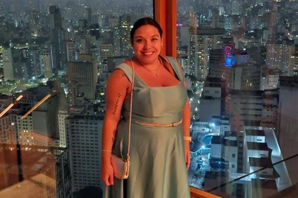 Foto colorida em tons de azul e vermelho, de uma mulher com vestido elegante, frente a um viro que mostra vários prédios na cidade de São Paulo - Metrópoles.