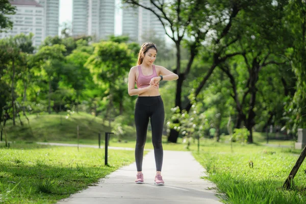 Mulher asiática olhando para seu relógio inteligente em um parque. Depois de correr ou caminhar para verificar a saúde. Metrópoles