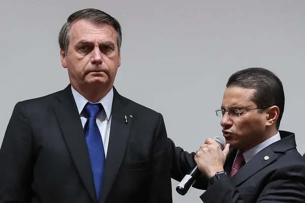 O presidente Bolsonaro recebe oração do deputado federal e pastor, Marcos Pereira. Ele fala em microfone, de olhos fechados, enquanto o presidente olha para frente - Metrópoles