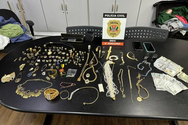 Imagem mostra joias, dinheiro e outros objetos apreendidos com uma dupla de criminosos sobre uma mesa da polícia - Metrópoles