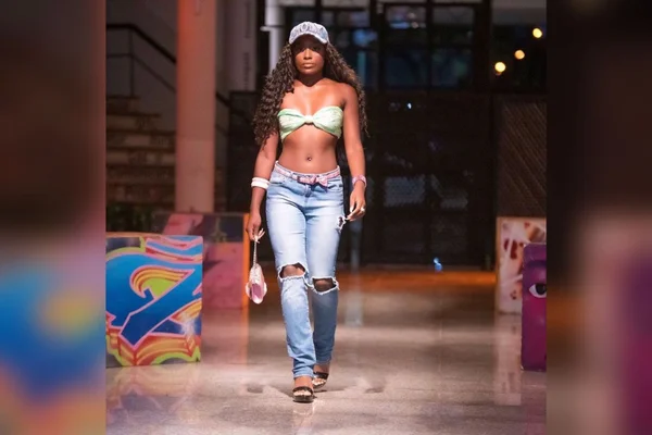 Mulher desfilando com calça jeans, bone e tope- Metrópoles