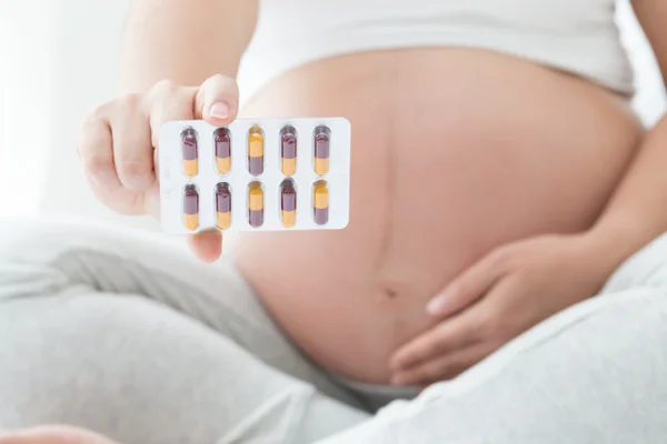 Mulher grávida segurando cartela de medicamentos ou remédios