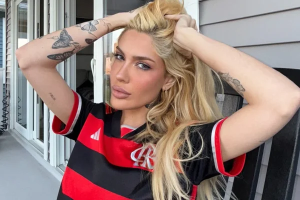 Karoline Lima com as mãos nos cabelos loiros e usando uma camisa do Flamengo